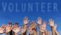 multi-ethnic volunteer group raising hands against blue sky