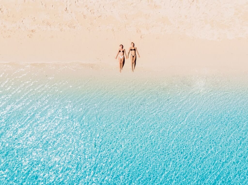 Couple of woman relaxing at paradise beach with blue sea. Aerial view