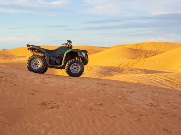 Quadracycle stands among the yellow sand dunes in the Sahara desert under the blue sky in Tunisia. Desert quad bike racing. Travel landscape with copy space