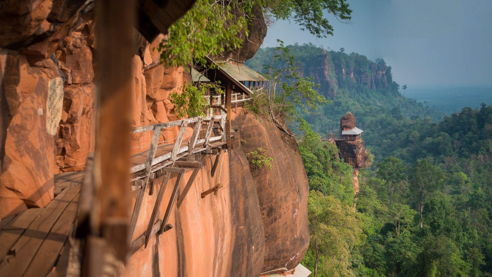 Wooden bridge and walkway attached to a red cliffside at Wat Phu tok mountain Bueng Kan, Thailand.