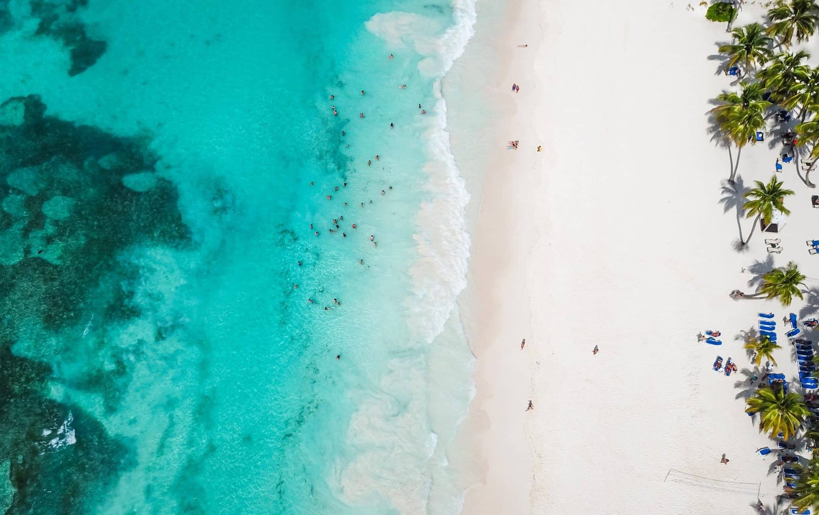 Incredible view of the white sandy beach from a bird's eye view. Top view of beautiful white sand beach with turquoise sea water and palm trees, aerial drone shot.