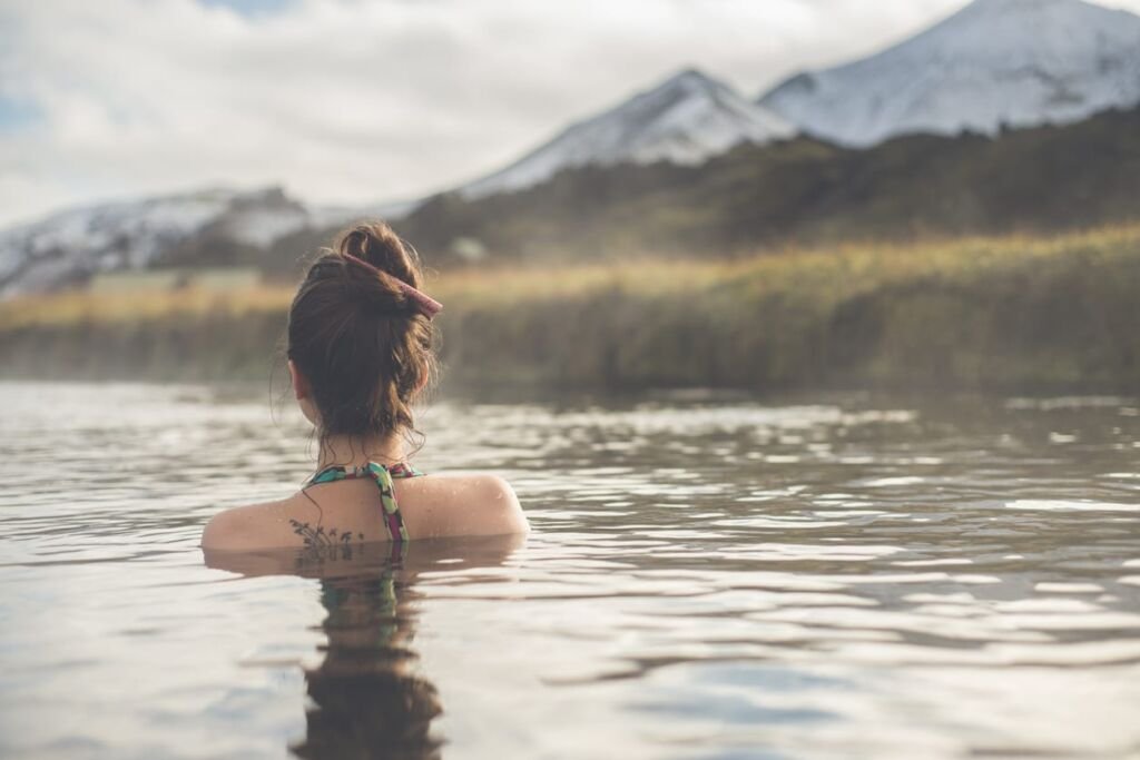 woman in a hot spring looking out at snow-capped mountains.