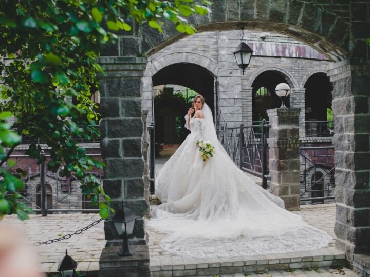 Young beautiful bride in luxury dress with a long train posing on the territory of country hotel