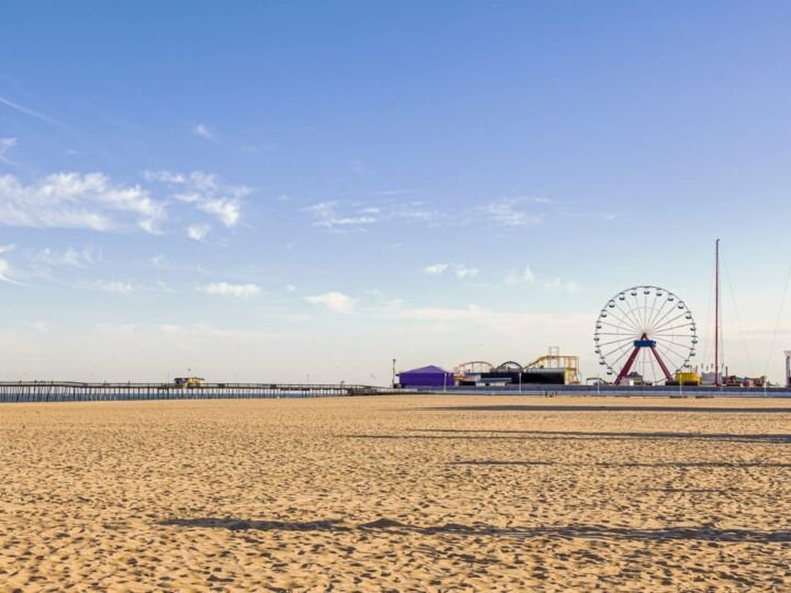 Empty beach of the popular tourist destination, Ocean City, Maryland. Image shows an afternoon view of the pier, board walk, shops, ferris wheel, lifeguard stands and the ocean at distance.