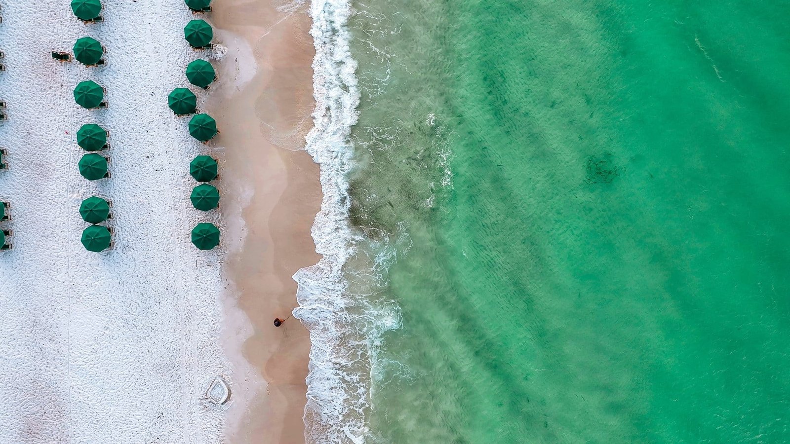 Tide breaking on Destin Beach. Emerald green waters in the morning as waves crash on Destin Beach. Fish swimming in low tide. Beach chairs and umbrellas set up in the morning for tourists and vacationers to relax on a Florida day.