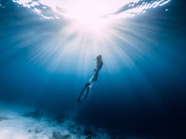 Woman freediver glides over sandy sea with fins