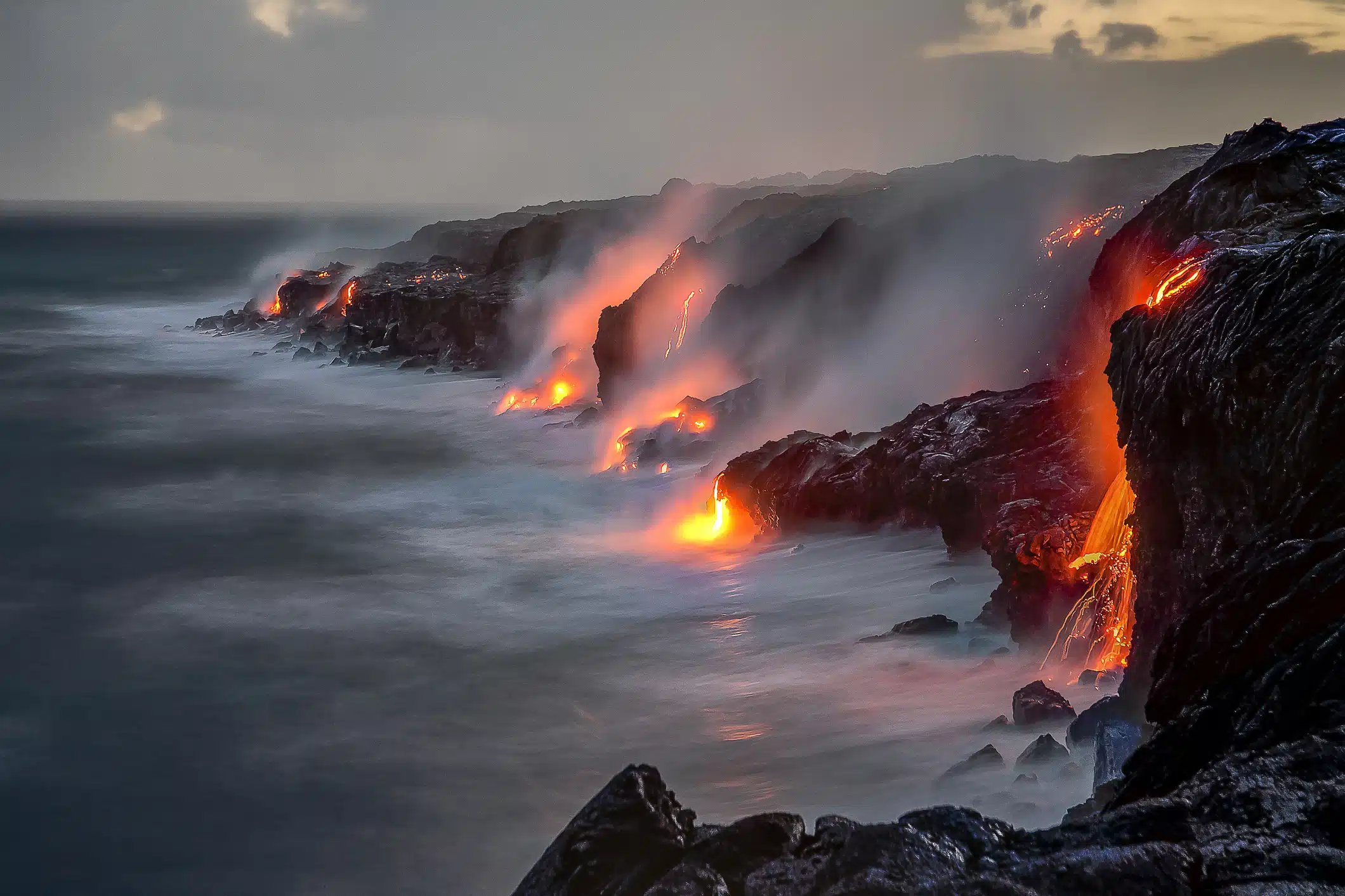 A series of lava flows spill into the ocean over a cliff at dusk, on the Big Island, Hawaii