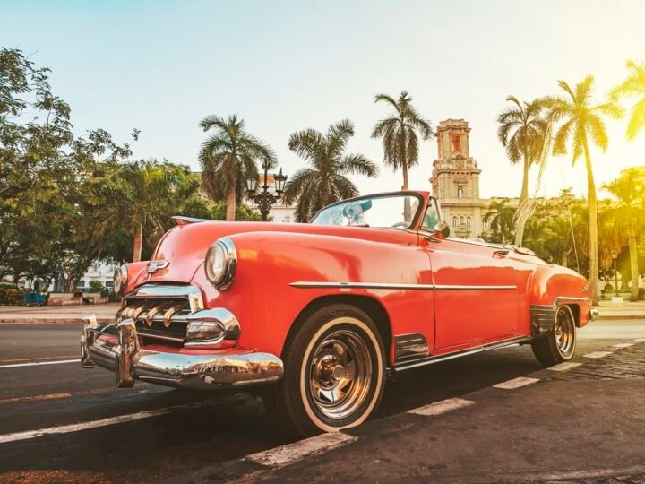 Classic American car against the background of palm trees in the bright sun in the evening in Havana against the background of colonial architecture