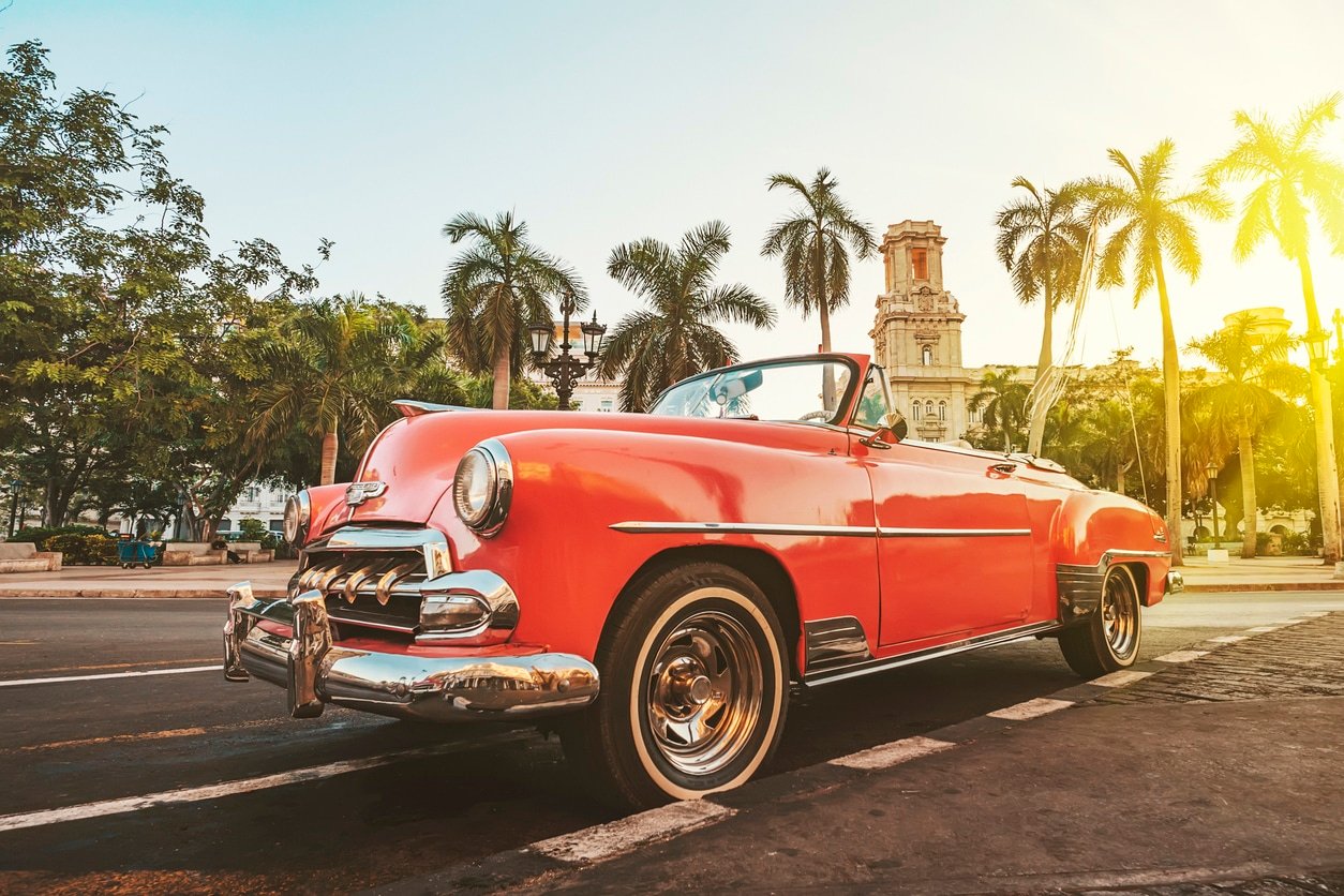 Classic American car against the background of palm trees in the bright sun in the evening in Havana against the background of colonial architecture