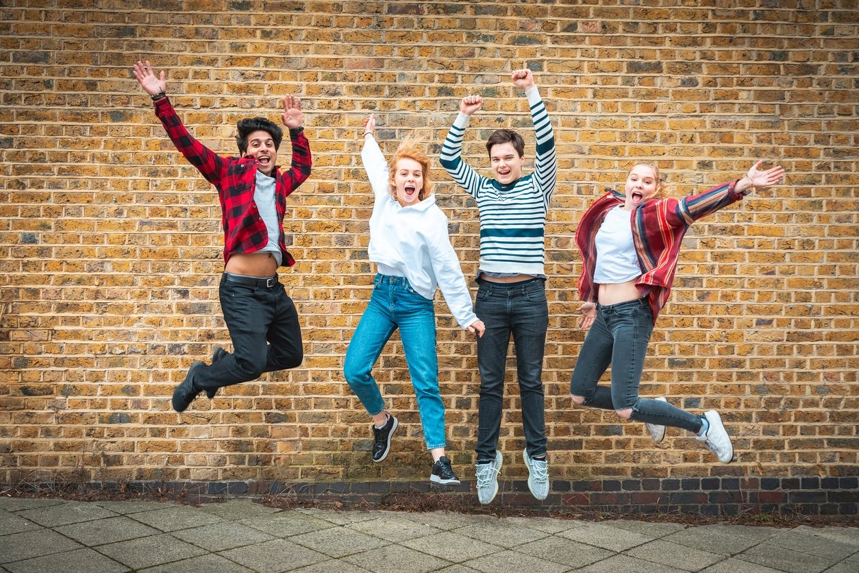 Happy teen friends jumping in front of a wall