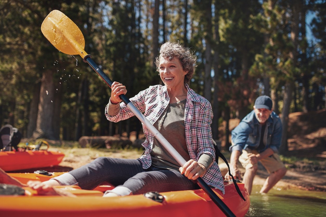 Portrait of happy senior paddling kayak in the lake with man supporting from behind. Mature couple enjoying a day at the lake.