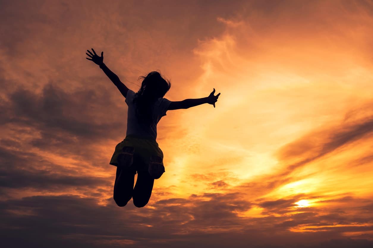 Silhouette young woman jumping outstretched hands in colorful sunset sky