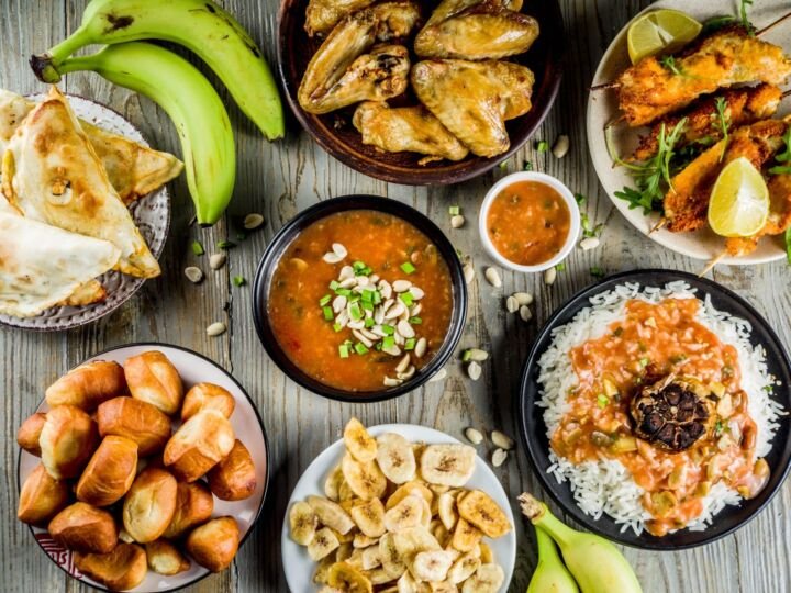 West african food concept. Traditional Wset African dishes assortment - peanut soup, jollof rice, grilled chicken wings, dry fried bananas plantains, nigerian chicken kebabs, meat pies, top view