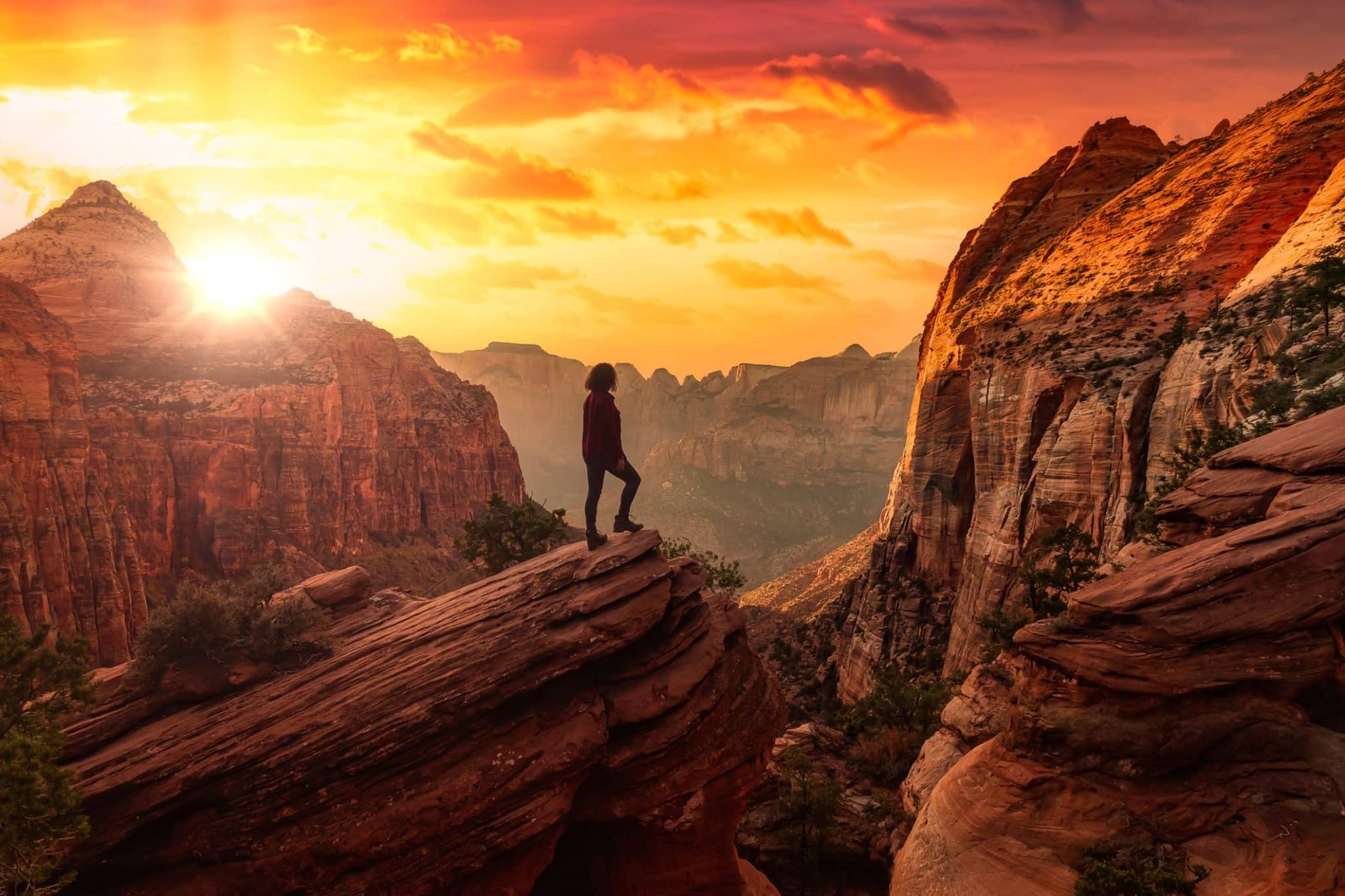 Adventurous Woman at the edge of a cliff is looking at a beautiful landscape view in the Canyon. Sunset Sky Art Render. Taken in Zion National Park, Utah, United States.