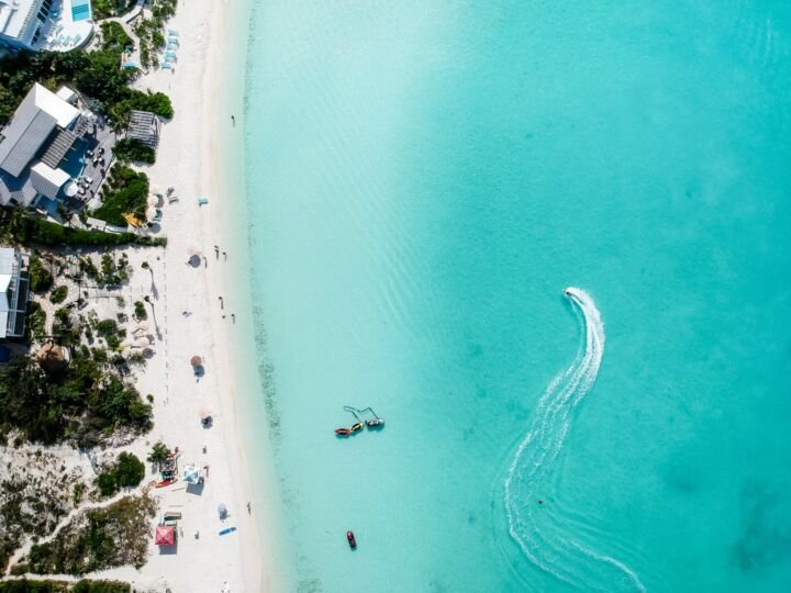 Drone photo of beach in Grace Bay, Providenciales, Turks and Caicos. The caribbean blue sea and underwater rocks can be seen, as well as some jet skies