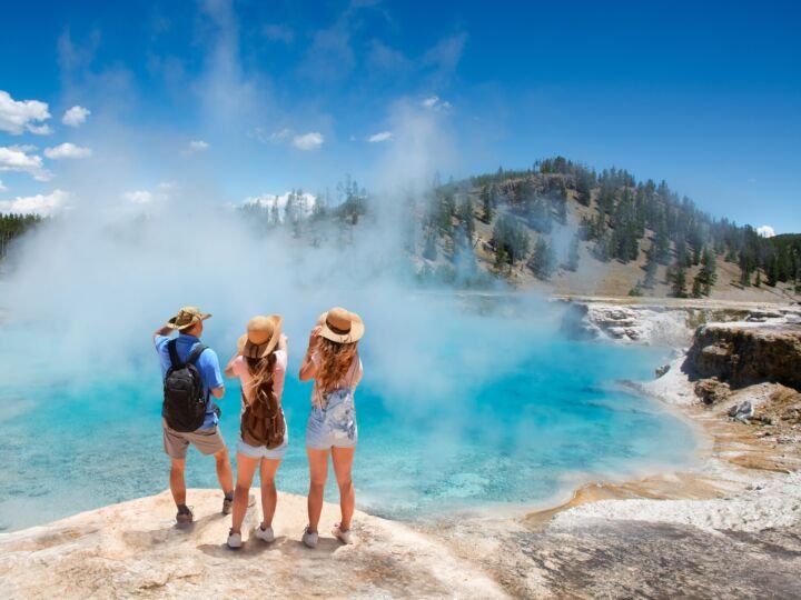 Family relaxing and enjoying beautiful view of gazer on vacation hiking trip. Friends on hiking trip. Excelsior Geyser from the Midway Basin in Yellowstone National Park. Wyoming, USA