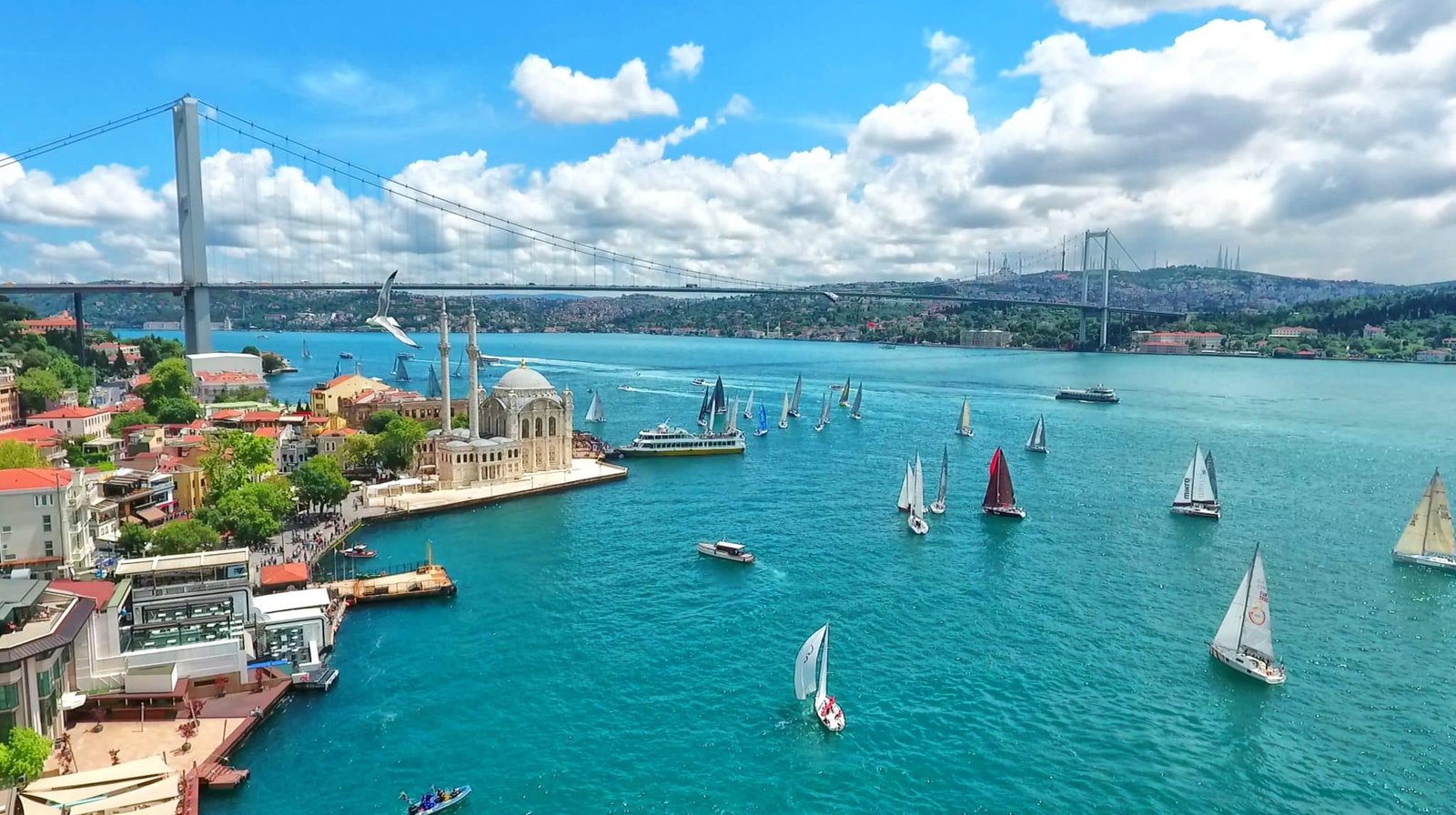 View of Istanbul Bosphorus with sailing boats passing under the bridge and mosque to the left hand side