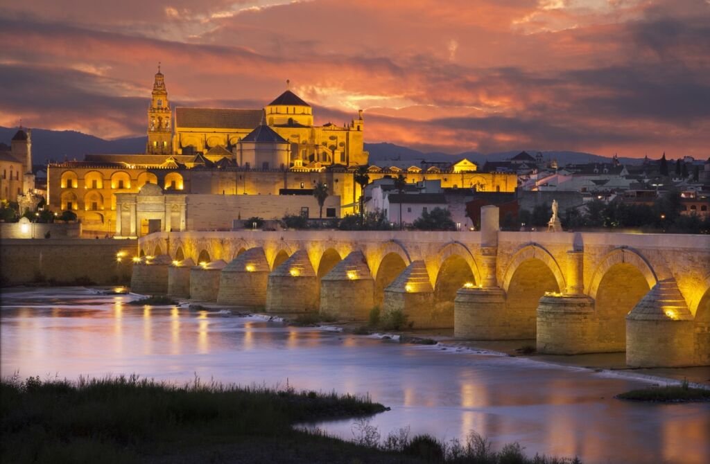 Cordoba - The Roman bridge and gate with the Cathedral in the background at evening dusk
