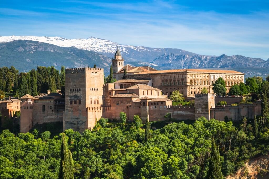 View of the famous Alhambra, Granada, Spain. Snow-capped mountains in the background, trees in foreground