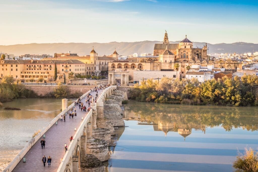 Nice old city of Cordoba with people crossing over the bridge and reflections on the river