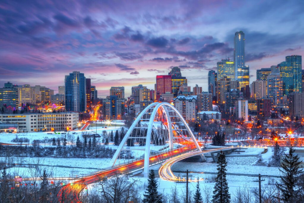 Light trails from rush hour traffic light up Edmonton downtown Winter sunset skyline showing Walterdale Bridge across the frozen, snow-covered Saskatchewan River and surrounding skyscrapers.