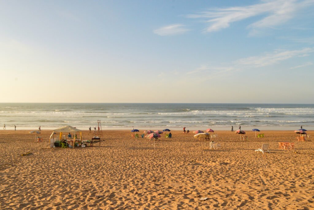 At La Corniche beach in Casablanca, the sun sets in a symphony of colors, casting a golden glow on the sand, while the waves softly kiss the shore under the painted sky.