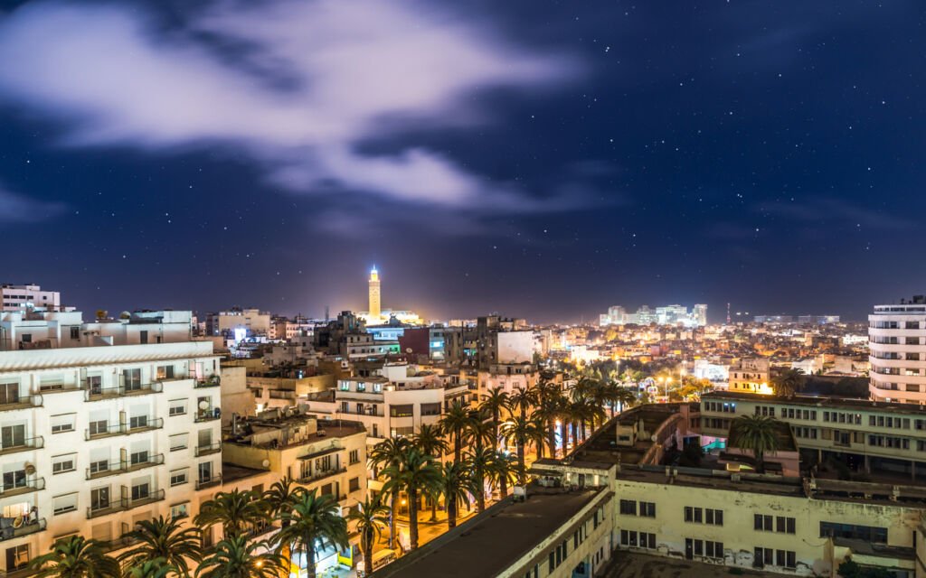 The vibrant cityscape of Casablanca unveils a stunning mosaic: the majestic Hassan II Mosque, bustling markets, and coastal skyscrapers against the backdrop of the Atlantic Ocean's shimmering expanse.