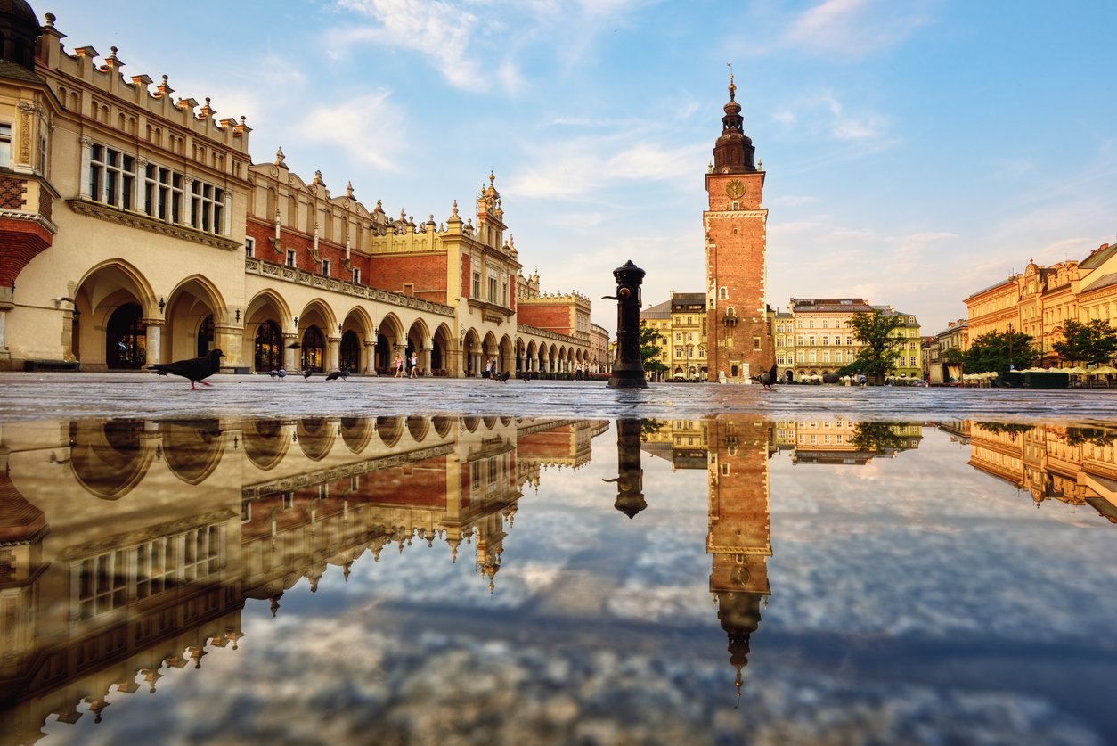 Cloth hall market and the Town Hall tower on Rynek main square in Krakow Old town, Poland, reflecting in the rain puddle