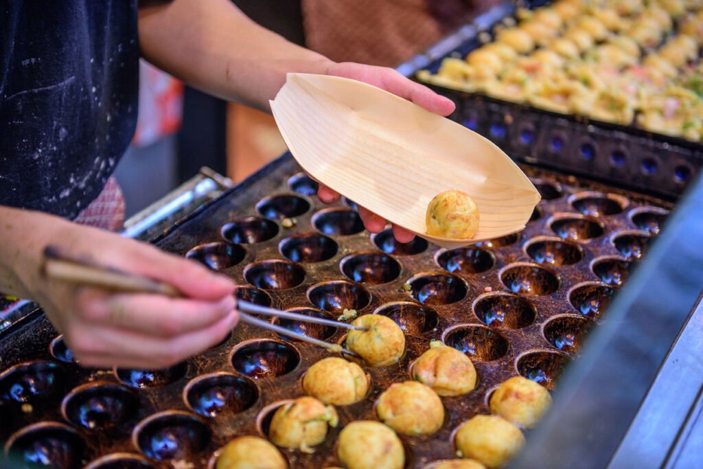 Osaka's street food scene enchants with tantalizing aromas, sizzling takoyaki balls, okonomiyaki pancakes, and friendly, bustling vendor stalls.