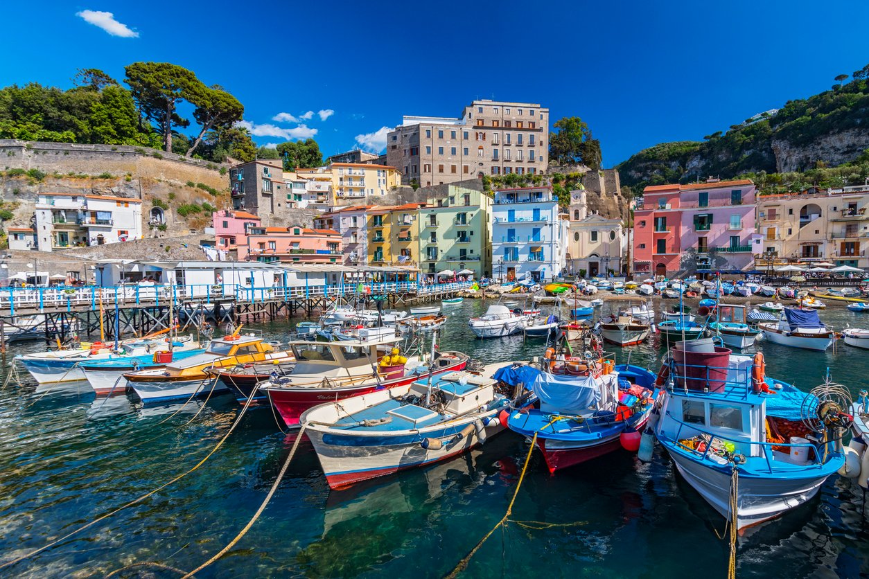 In Sorrento's Marina Grande, quaint fishing boats bob gently, their colorful hulls reflecting in the clear waters. The essence of Amalfi Coast's maritime charm captured in a tranquil harbor.