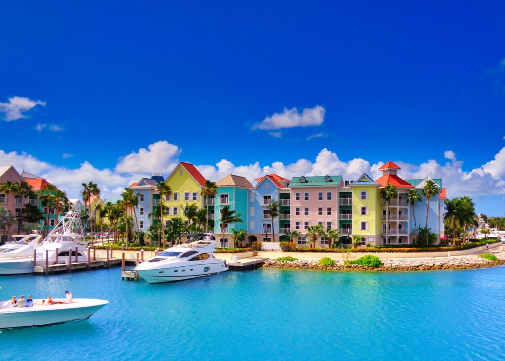 Nassau's waterfront dazzles with pastel-hued houses, a vibrant symphony of peach, mint, and azure, nestled along the shoreline like a dreamy coastal palette painted against the Bahamian sky.