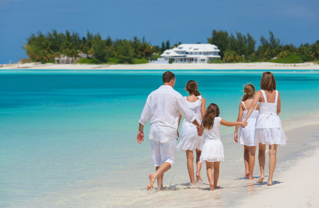 A happy young Caucasian family, dressed in white, strolls along a tropical beach by the ocean on a Caribbean island. Joyful moments blend with the rhythmic serenade of the waves.