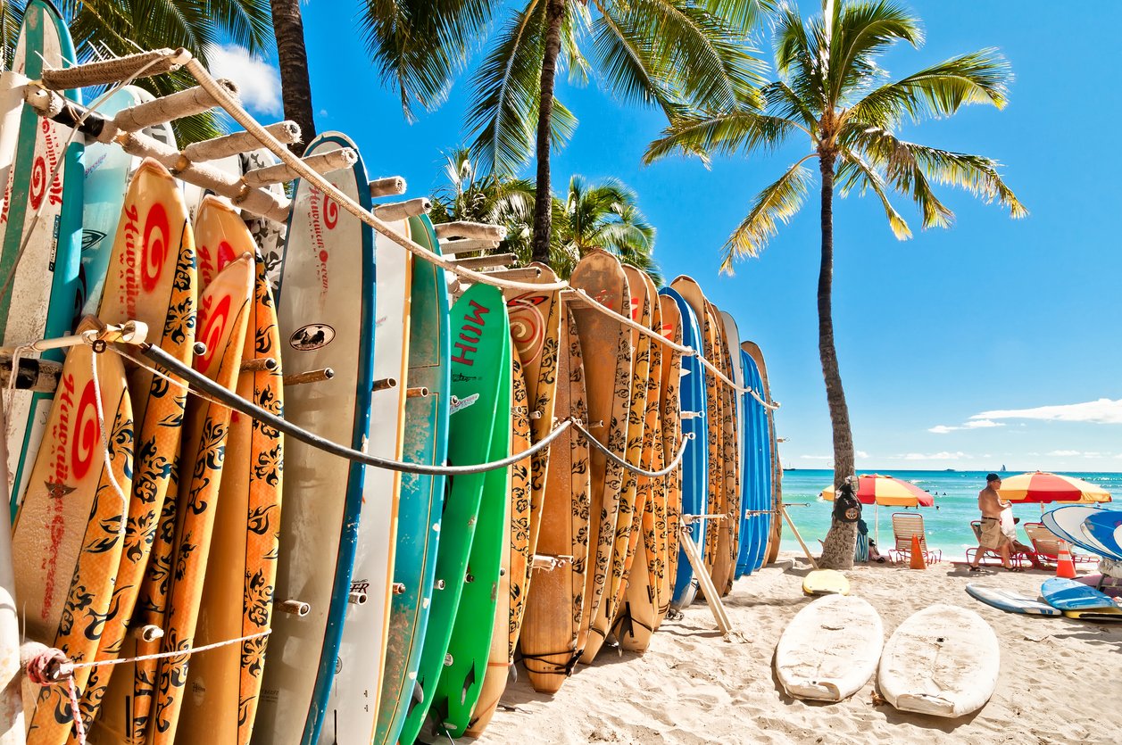 Waikiki's vibrant charm encapsulated—surfboards stand sentinel in a rack, a kaleidoscope of colors against the backdrop of Honolulu's iconic beach. Oahu's spirit captured in a single coastal scene.