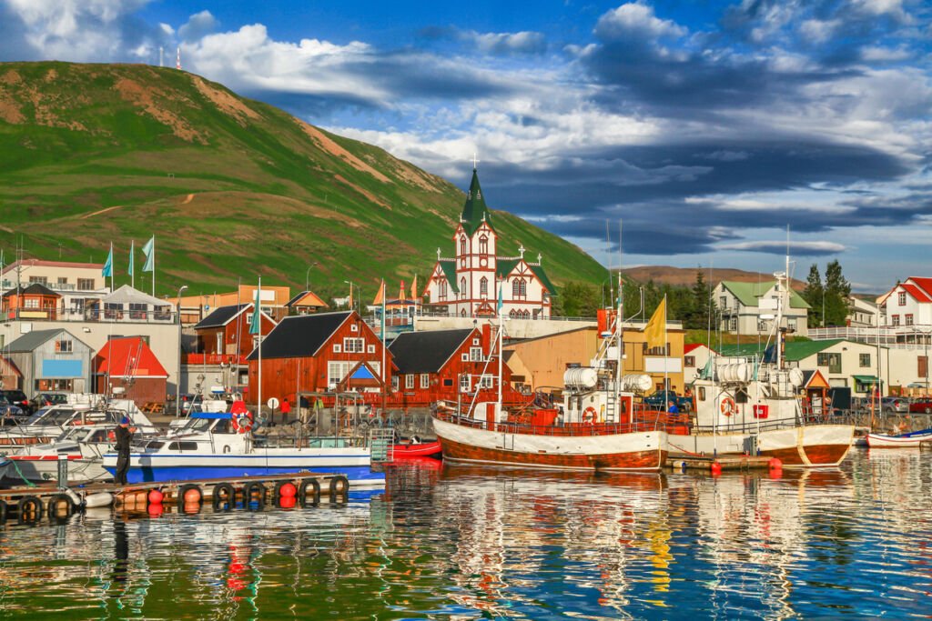 Husavik, bathed in golden sunset hues, exudes historic charm. The tranquil north coast of Iceland frames this picturesque town, where the soft evening light paints a mesmerizing Nordic panorama.
