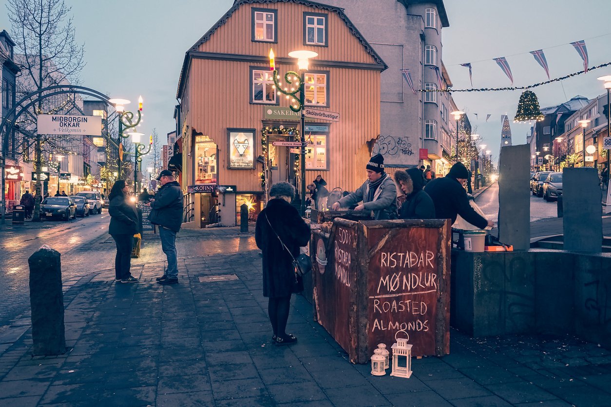 Reykjavik, Iceland sparkles with winter magic. Panoramic cityscape, vibrant main streets, and a Christmas street food stall. Unidentified figures stroll, indulging in festive shopping, immersed in the holiday spirit.