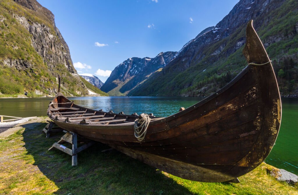 A Viking ship rests by the serene Gudvangen Fjord in Norway, echoing ancient tales. The vessel, a sentinel of history, mirrors the tranquil beauty of its scenic Nordic surroundings.