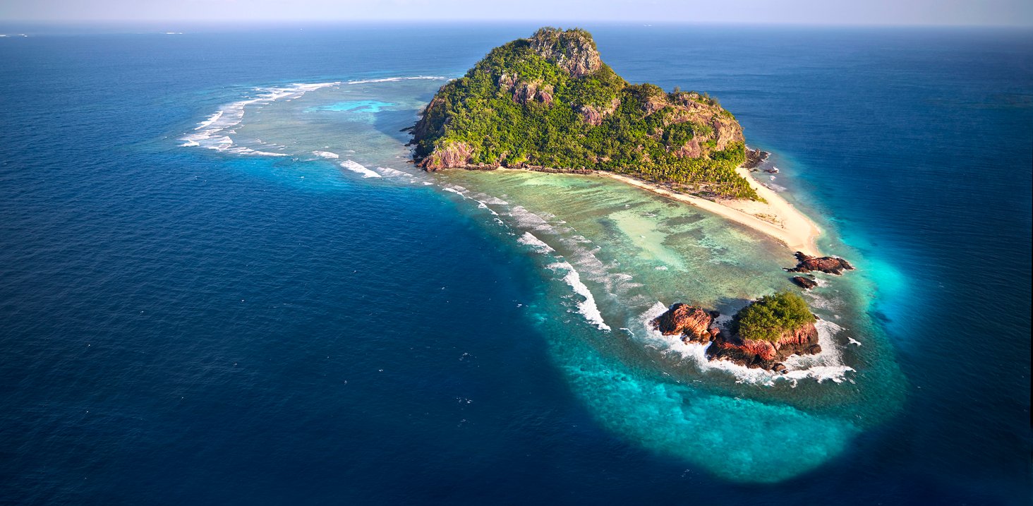 Aerial view of a tropical Fiji island reveals a paradise of emerald forests, ivory beaches, and crystal-clear lagoons, where nature's artistry and the ocean's allure converge in harmony.