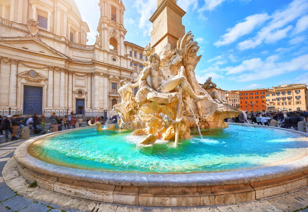 Rome's Piazza Navona bathed in summer sun. The Fountain of the Four Rivers, a Baroque masterpiece by Bernini, adorns the square. Ancient statues, an obelisk, and Sant'Agnese in Agone church grace this iconic landmark.