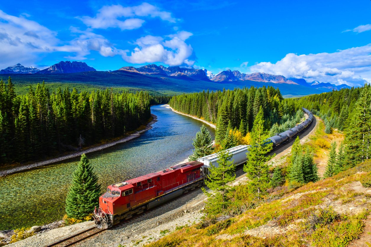 Autumn's splendor unfolds as a majestic train traverses Morant's Curve in Banff National Park. The Canadian Rockies embrace the rhythmic passage, a symphony of nature and engineering marvel.
