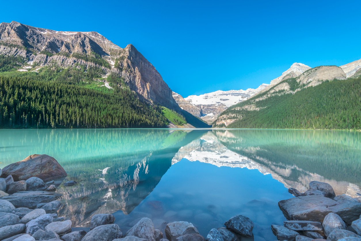 Banff National Park, Alberta, Lake Louise mirrors the turquoise sky, cradled by pine-clad mountains. Victoria Glacier looms majestically, etching a timeless spectacle of Canadian wilderness beauty.
