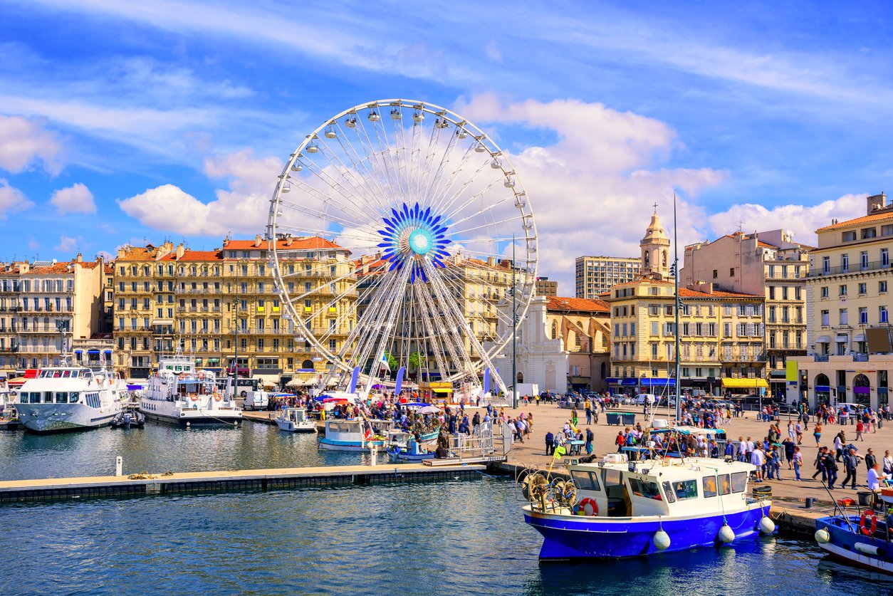 Marseille's Vieux Port promenade dances with life. Quayside cafes beckon amidst the lively bustle. Sailboats sway in rhythm with the Mediterranean breeze, framing a scene of coastal allure.