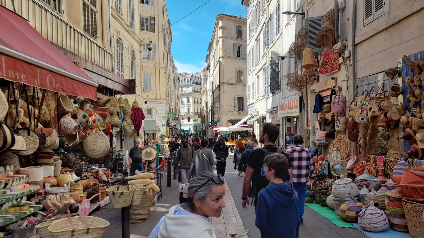 Marseille's fruit market awakens with a burst of colors. Straw baskets and bags, a vibrant mosaic against the azure sky, lure in bustling shoppers on the French Riviera.