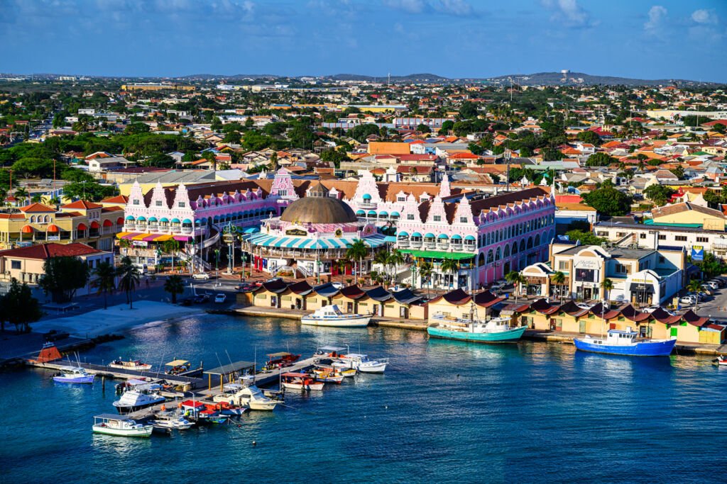 Oranjestad's waterfront captivates with vibrant hues reflecting in the Caribbean waters, as pastel-hued buildings line the shore, creating a picturesque scene of serenity and tropical charm.