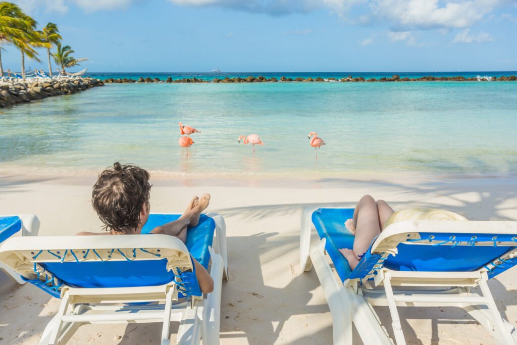 A young couple finds tranquility on Flamingo Beach in Aruba, the soft sands and azure waters providing a serene backdrop for their relaxation and moments of shared bliss.