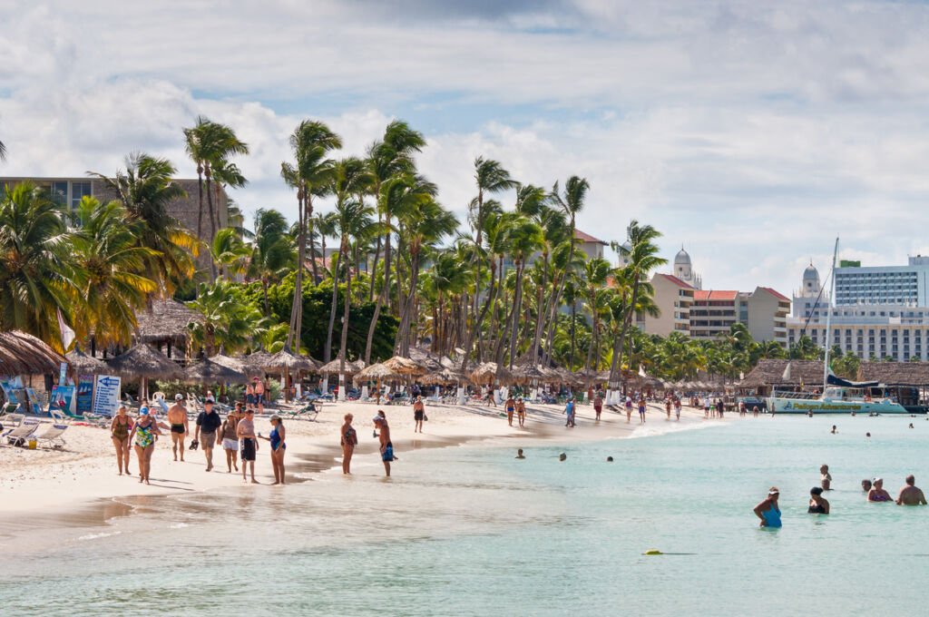 Oranjestad, Aruba: Beachgoers enjoy the sun and sea on the renowned Palm Beach, creating a lively scene of relaxation and water activities in the idyllic surroundings of Aruba.
