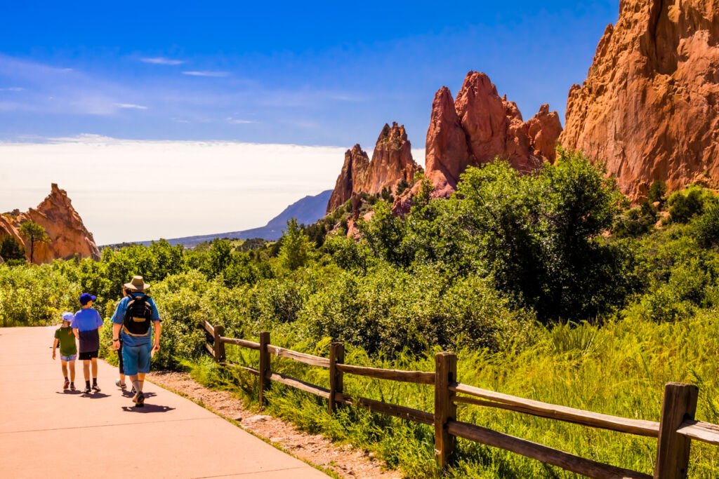 In the summer, Garden of the Gods Park in Colorado Springs offers a stunning panorama. A family strolls along a winding footpath, immersed in the park's natural beauty and iconic rock formations.