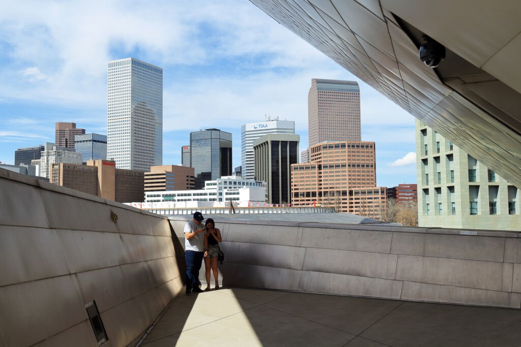 In Denver, Colorado, a couple captures moments on a deck, framed by the downtown cityscape. Love and urban charm converge, creating a picturesque scene against the city's skyline.