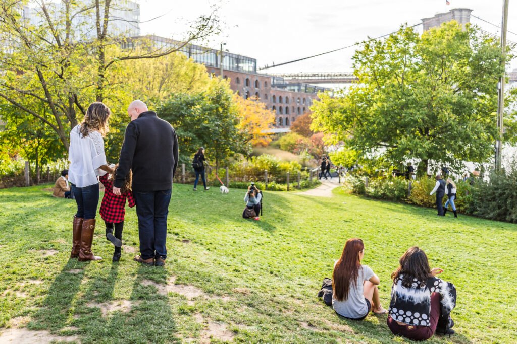 In Brooklyn's Dumbo district, families enjoy the green spaces of Main Street Park, with the iconic bridge framing the urban landscape, a serene escape in bustling New York City.