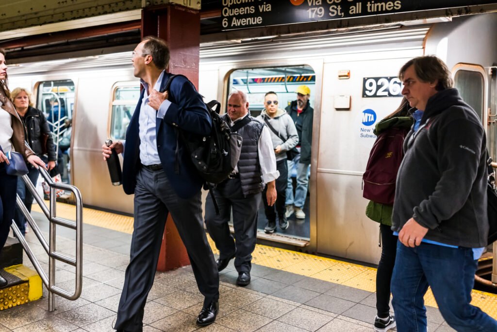 In a New York City subway station, businesspeople stream onto the platform after work, joining the bustling throng of commuters during rush hour, a quintessential scene of urban transit.