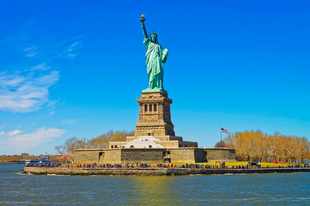 On Liberty Island, in Upper New York Bay, stands the Statue of Liberty, an enduring symbol of freedom. Tourists stroll, captivated by its grandeur, in New York City, USA.